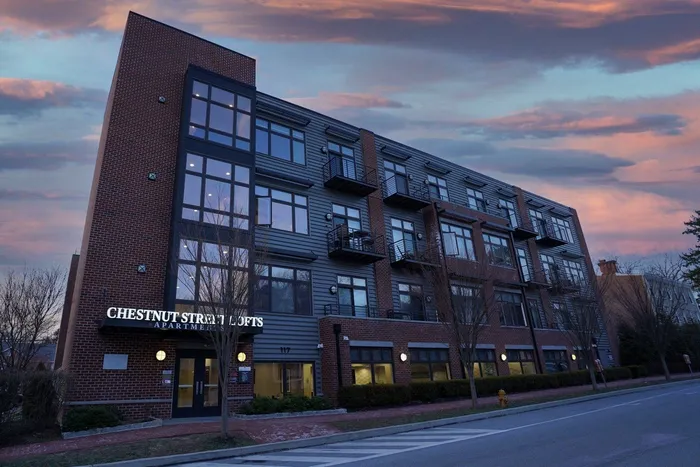 One-Bedroom Apartments in West Chester, PA - Chestnut Street Lofts - Street View of Apartment Building with Property Signage, Double Doors, Glass Windows, Balconies, Brick Sidewalk, and Trees.