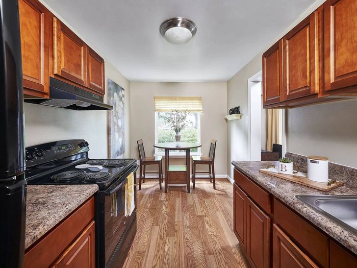 1-Bedroom Apartments in Frederick, MD - Willowdale Crossing - Kitchen with Wood-Style Flooring, Black Appliances, Wooden Cabinetry, Granite Countertops, and View of Dining Area.