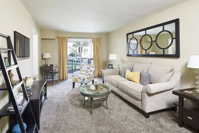Pet-Friendly Apartments In Frederick, MD - Willowdale Crossing - Living Room With Carpet Flooring, Couch, Chair, Side Tables With Lamps, Glass-Top Coffee Table, And Sliding Glass Door