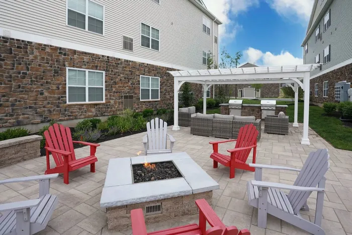 Middletown, PA, Apartments - Woodland Hills - Grilling Area with Fire Pit, Wooden Adirondack Chairs, Pergola Lounge Seats, and Grill Stations.