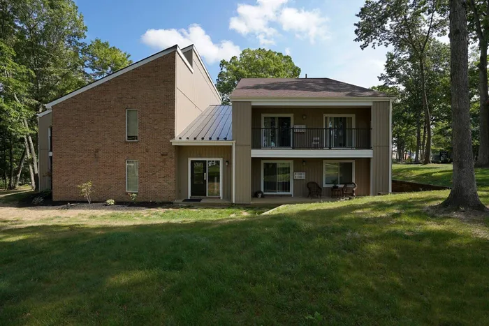 State College, PA, Apartments for Rent - Toftrees - Property Exterior with Tan Walls, White Trim, Windows, Balcony, Grassy Lawn, Trees, and Concrete Path.