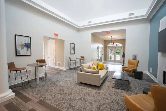 Pittsburgh, PA Apartments - Bear Run Village - Clubhouse with a Pool Table, Blue Accent Wall, Mounted TV, High-top Seating and White Table, Large Windows, Kitchen Area with White Countertops, Mounted Shelving, Cooking Island with a Sink, Seating, and Hanging Lights, and a Mounted Clock