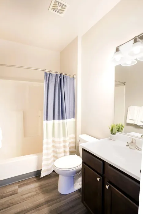 Pittsburgh, PA Apartments Near PNC Park - Bear Run Village - White Bathroom with Tub and Shower, Wood-Style Flooring, Large Mirror, Vanity with Wooden Cabinetry, Sink, and White Countertop