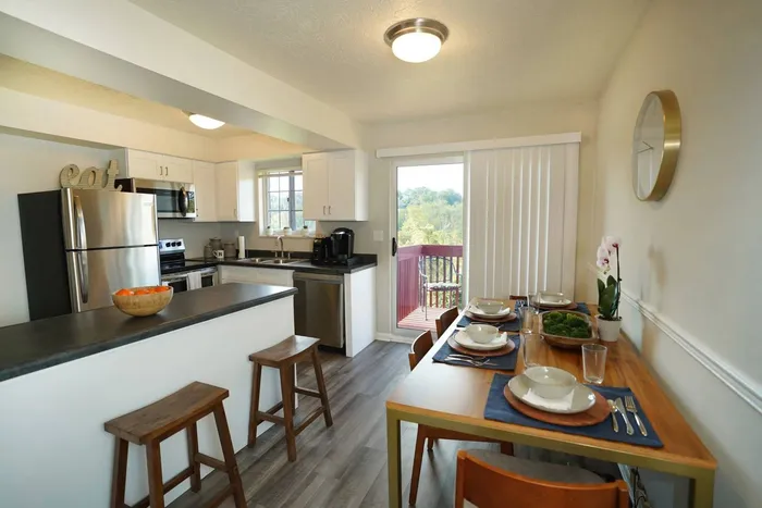 Jefferson Hills, PA Apartments For Rent - Heritage Hills - Open Concept Kitchen and Dining Area, with Stainless Steel Appliances, Black Countertops, White Cabinetry, and Sliding Glass Door to Balcony