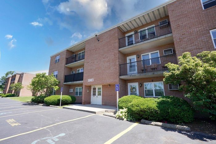 Three-Bedroom Apartments in Altoona, PA - Walton Heights - Brick Exterior Showcasing Spacious Balconies with Black Railings, Manicured Bushes, and Parking Lot.