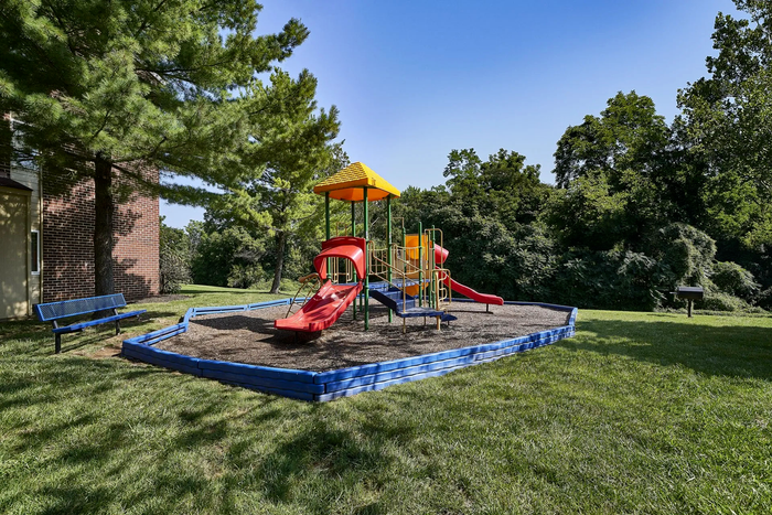 Frederick, MD Apartments - Willowdale Crossing - Outdoor Playground Near Apartment Building With Seating Bench And Surrounded By Well-Maintained Grass And Lush Trees