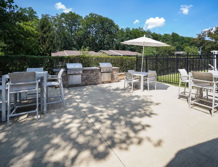 Apartments in West Chester, PA, for Rent - Goshen Terrace - Grilling Station with Umbrella Tables, Chairs, Hedgerow, and Manicured Lawn.