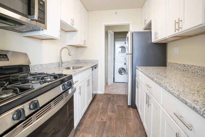 Apartments for Rent in Allentown, PA - Regency Towers - Kitchen with Wood-Style Flooring, Stainless-Steel Appliances, White Cabinets, and View of Laundry Closet with Stacked Washer and Dryer.