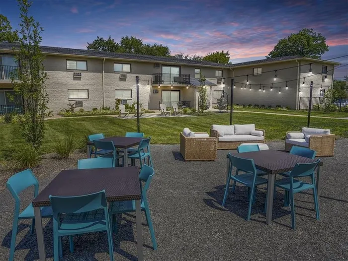 Pet-Friendly Apartments in West Chester, PA - Goshen Terrace - Courtyard with Tables and Charis, Outdoor Couch and Armchairs, String Lights, and View of Apartment Building.