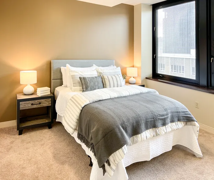 Apartments in Pittsburgh for Rent - Apartments at River View - Bedroom with Plush Carpeting, a Large Window with Black Trim, and Accent Wall