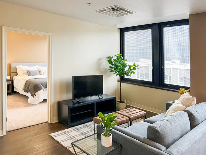 Pet-Friendly Apartments in Pittsburgh, PA - Apartments at River View - Furnished Living Room with Hardwood Flooring, Large Windows with Black Trim, and a Door to the Bedroom with Carpet Flooring