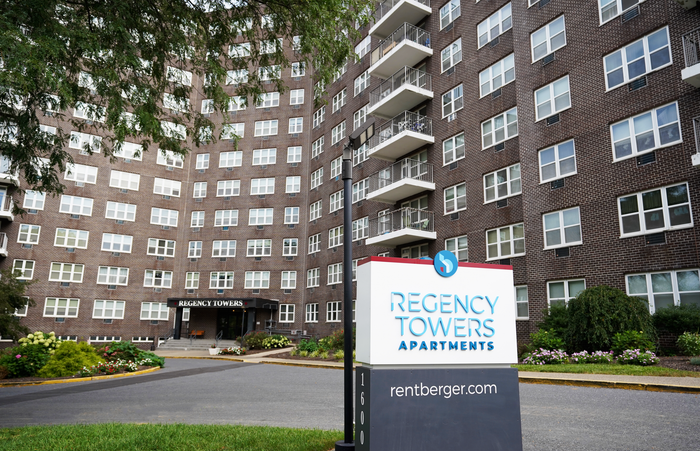 Allentown, PA, Apartments - Regency Towers - Property Driveway with Signage, Apartment Building, Manicured Grass, and Bushes.