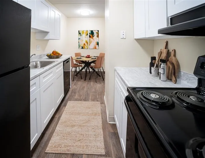 One BR Apartments in Wilmington DE - Chestnut Run Village - Kitchen with Wood-Style Flooring, Black Appliances, White Marble Countertops, and White Cabinetry