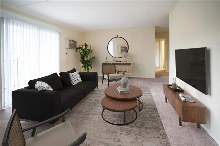 Pet Friendly Apartments in Wilmington DE - Chestnut Run Village - Living Room With Tan Walls, Black Couch, Armchairs, Coffetable, Area Rug Over a Carpetted Floor, TV, Large Window with Vertical Blinds, AC Unit, and Houseplant