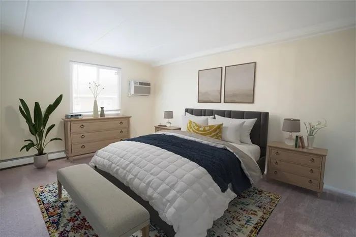 Wilmington, DE Apartments - Chestnut Run Village - Bedroom with Full-Sized Bed, Bed Bench, Carpet, Wall Art, Light Wood Dresser, AC Unit, Potted Plant, and Window