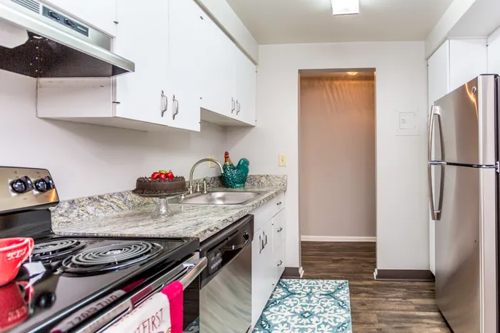 Small apartment kitchen with white cabinets, granite coutner tops, and stainless steel appliances.