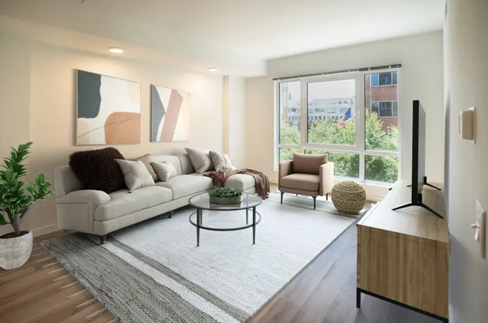 Apartments for Rent in Lancaster, PA - 202 Queen - Living Room with Wood-Style Flooring, Area Rug, Sectional Couch, Wall Art, Glass-Top Round Coffee Table, Armchair, Media Cabinet, TV, and Floor-to-Ceiling Windows.