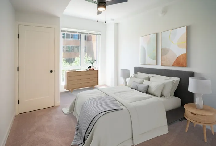 Apartments in Lancaster, PA, for Rent - 2020 Queen - Bedroom with Carpeted Flooring, Large Bed, Wall Art, Round Nightstands with Lamps, Ceiling Fan, Dresser, and Floor-to-Ceiling Windows.