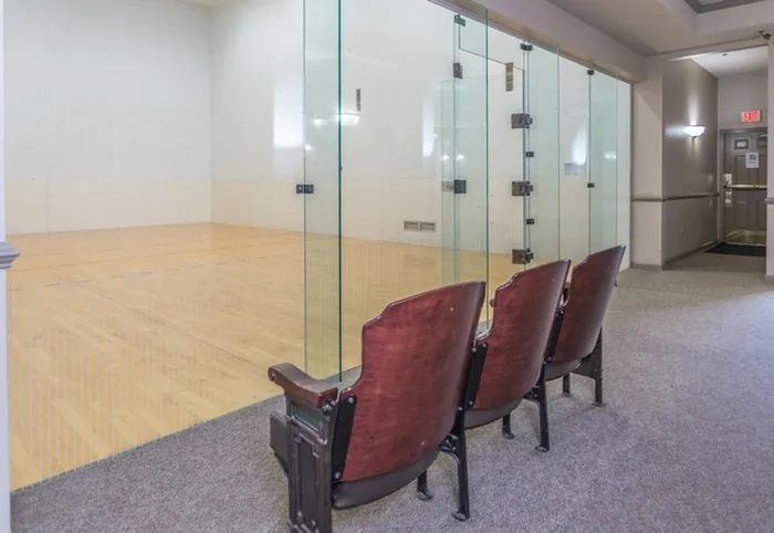 Three red chairs in front of a glass wall for the indoor racquetball court.