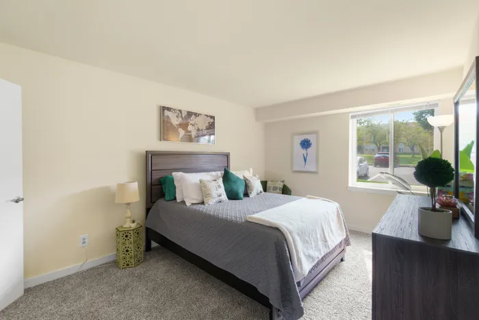 Comfortably furnished neutral bedroom with a queen-size bed and natural light.