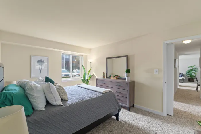 Furnished neutral bedroom with a queen-size bed and large bureau.