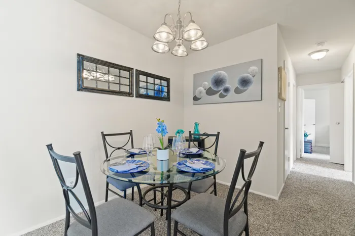 Close-up view of a round glass dining table with four chairs in a grey apartment dining area.