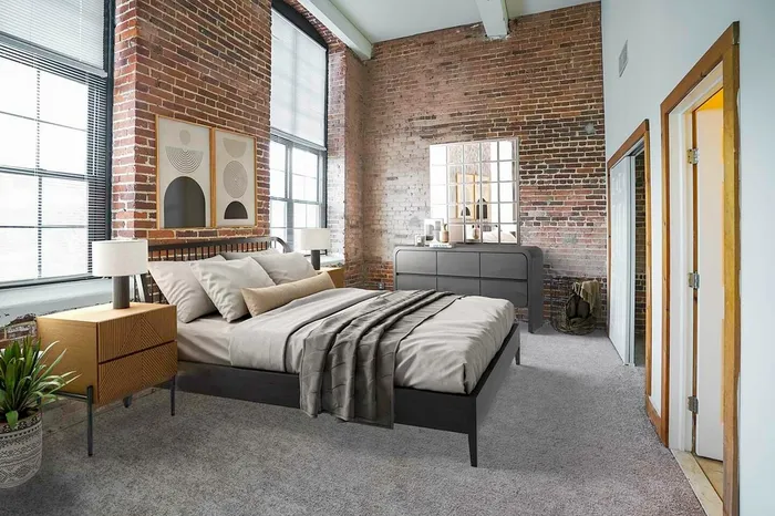 Apartments Near Da Vinci Science Center - The Mill - A Carpeted Bedroom with Brick Accent Walls, a Queen Sized Bed, and a Mirror-Dresser Set