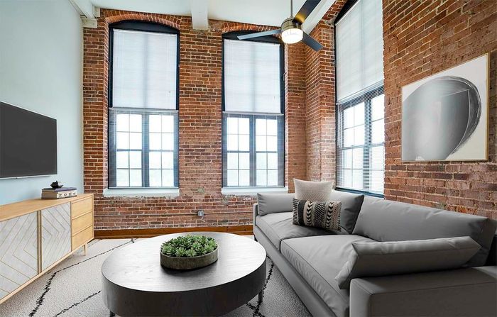 Apartments Near Lehigh Valley Zoo in Allentown, PA - The Mill - Living Room with a Large Grey Sofa, a Ceiling Fan, and Oversized Windows Allowing Natural Light