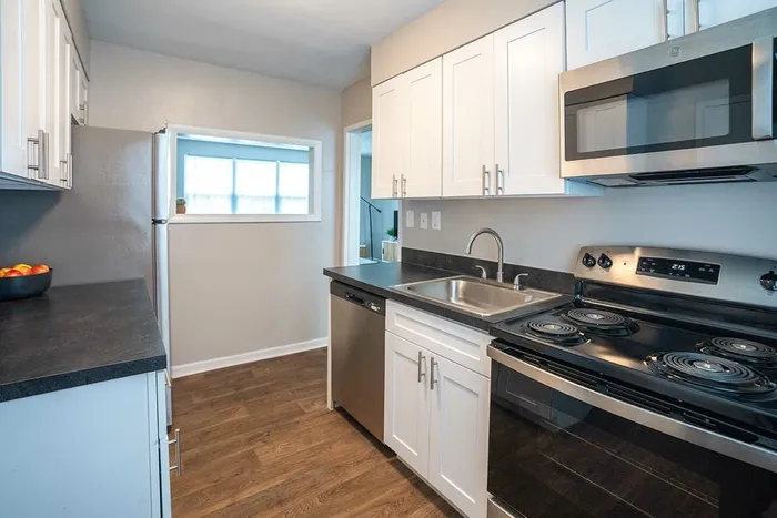 3-Bedroom Apartments in Wilmington, DE - Greenview at Chestnut Run - Modern Kitchen with Wood-Style Flooring, Black Countertops, White Cabinetry, and Stainless Steel Appliances.