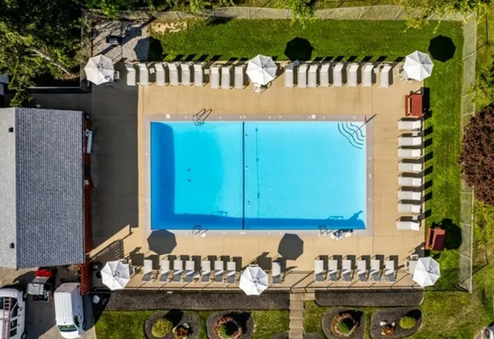 Apartments For Rent Jefferson Hills, PA - Heritage Hills - Gated Pool with Surrounding Greenery, Trees, Poolside Seating, and White Umbrellas