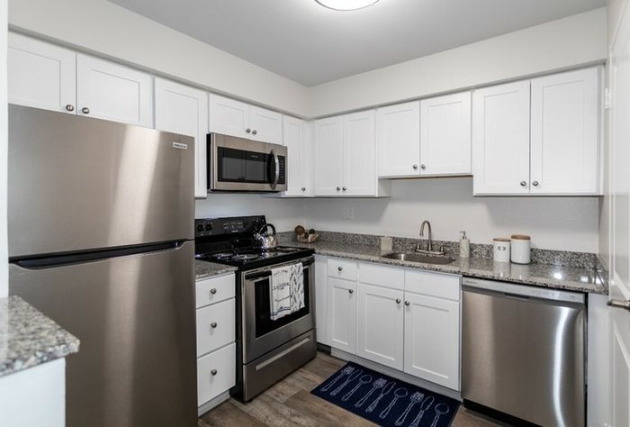 Two-Bedroom Apartments in Bensalem, PA - Village Square - Kitchen with Wood-Style Flooring, Granite Countertops, Stainless Steel Appliances, and White Cabinetry.