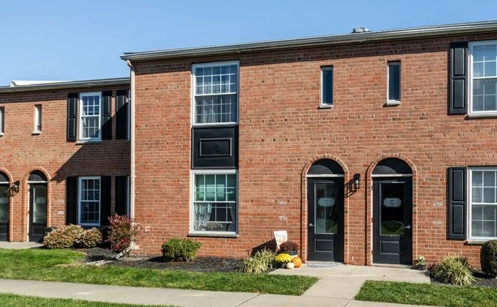 1-Bedroom Apartments in Bensalem, PA - Village Square - Brick Property Exterior with White Trim, Windows, Black Shutters, Manicured Bushes, and Surrounded by Grass Lawn.