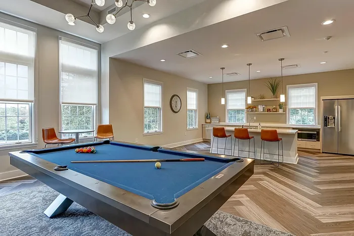 Dog-Friendly Apartments in Pittsburgh PA - Bear Run Village - Indoor Lounge Seating Area with High-top Seating with Round Tables, Grey Carpet Over Wood-Style Flooring, Cream Sofa, Leather Tan Armchairs, Coffee Table, Side Table, and TV with Fire Place