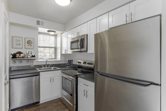 1 BR Apartments in Boothwyn, PA - Willowbrook - Furnished Bedroom with Carpeted Floor, Bed, Wooden Nightstand and Dresser, Windows and Decor.