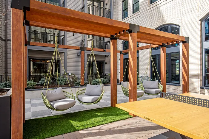 Contemporary outdoor lounge with comfortable swing chairs under a wooden pergola in a stylish apartment complex.