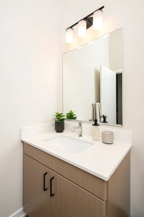 Modern bathroom vanity with sleek white countertop, a large mirror, and stylish lighting.