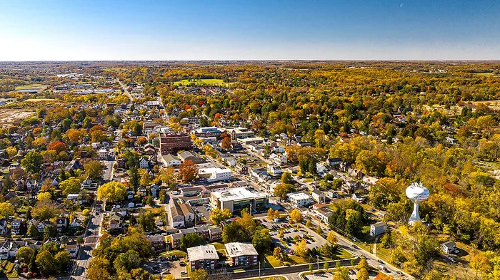 Aerial view of a picturesque town surrounded by lush autumn foliage under a clear blue sky.