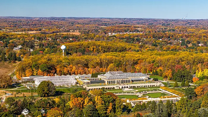 Aerial view of a grand estate surrounded by vibrant autumn foliage and sprawling gardens.