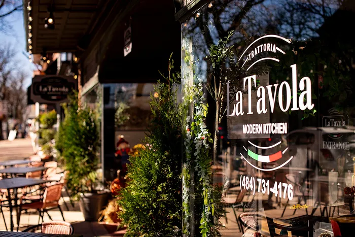 Charming exterior of La Tavola modern kitchen with outdoor seating and lush greenery.