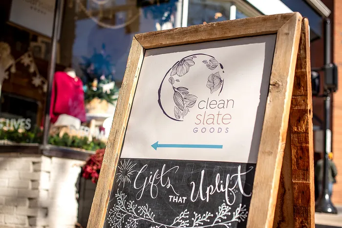 Rustic wooden sign outside a shop displaying 'Clean Slate Goods' with a decorative floral logo.