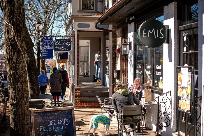 Lively street scene with a cozy cafe, outdoor seating, and people enjoying a sunny day.