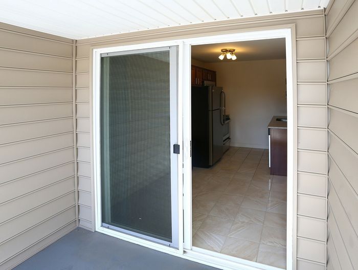 View of a modern kitchen through a sliding glass door from a patio area with beige siding.