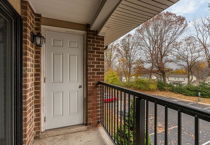 Inviting balcony with brick accents and scenic view of lush trees and suburban landscape.