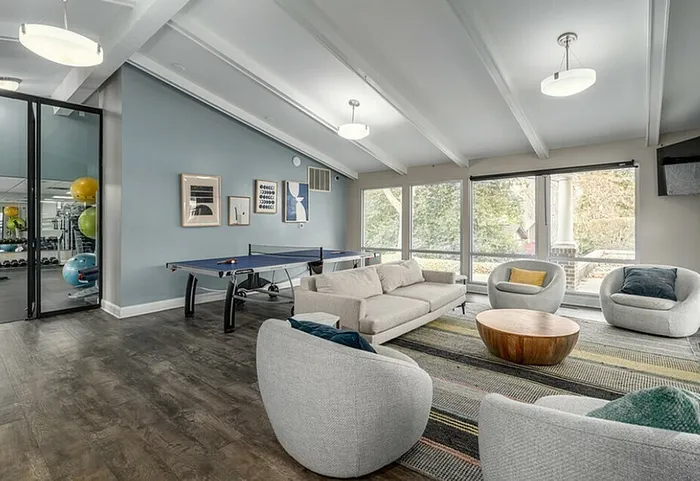 Spacious lounge featuring modern seating, large windows with natural light, and a ping pong table.