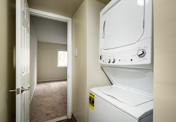 Efficient laundry area with a stacked washer and dryer set adjacent to cozy bedroom with carpet flooring.