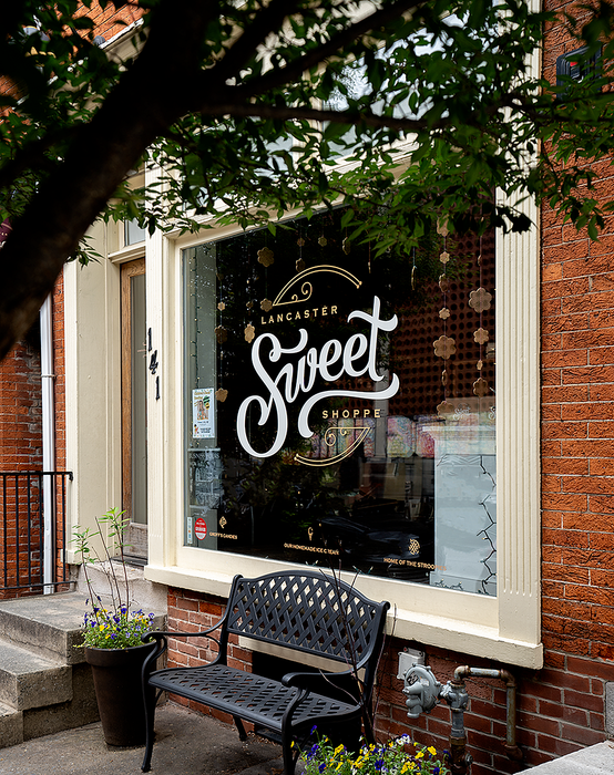 Charming exterior of a sweet shop with decorative window signage and a welcoming bench.