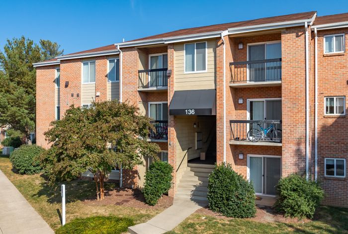 Bright and welcoming three-story brick apartment building with balconies and lush green surroundings.