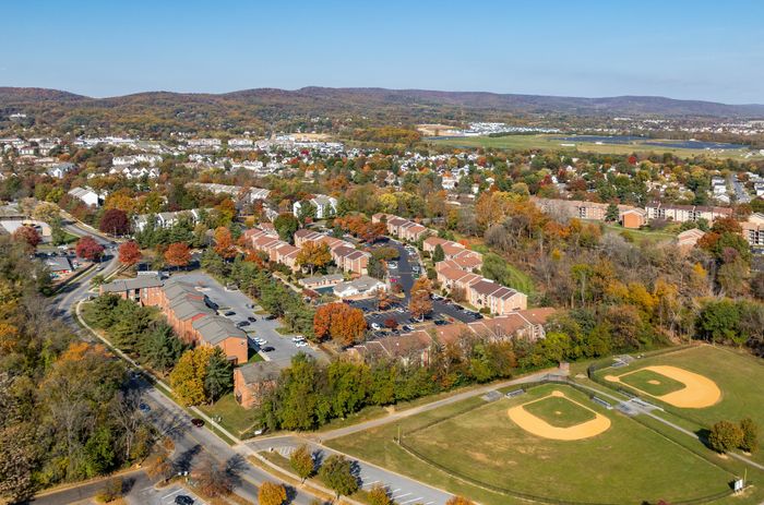 Aerial view capturing a vibrant community with residential buildings, surrounded by lush autumn trees and adjacent sports fields.