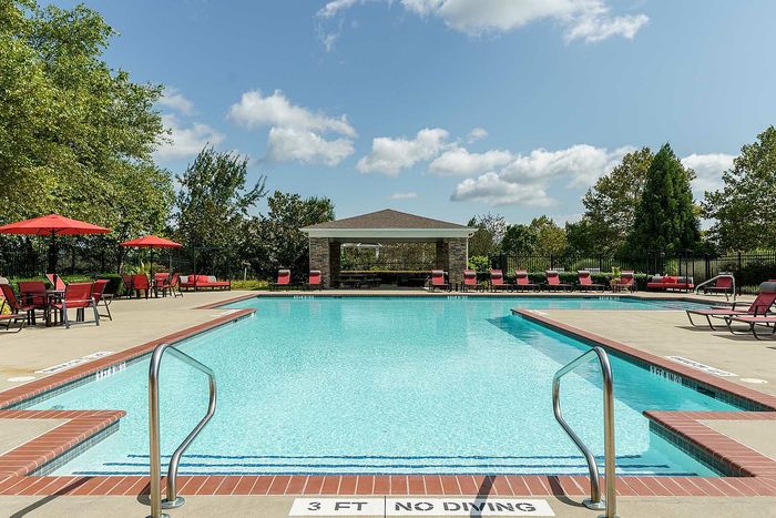 Inviting outdoor pool with red lounge chairs and umbrellas set against a lush green backdrop.