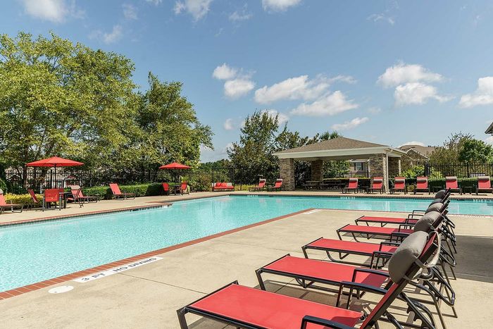 Inviting residential swimming pool with vibrant red lounge chairs and shaded seating area under a clear blue sky.